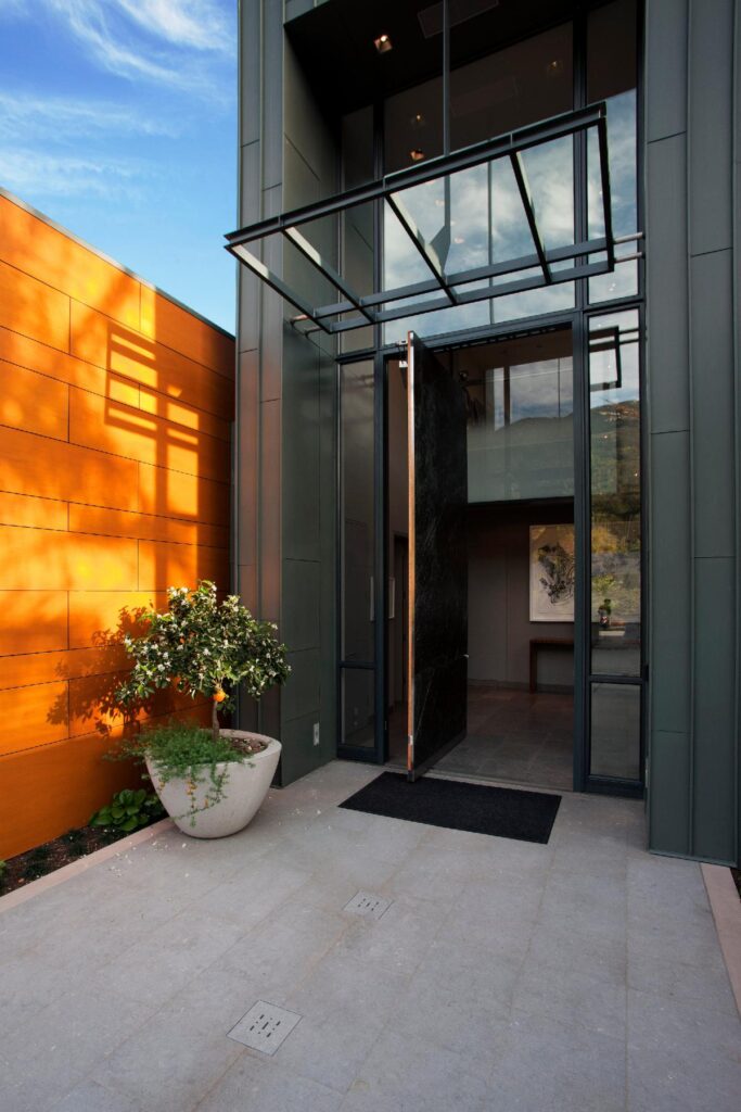 Steel windows and doors application at the entrance to a building, with a plant and sun-drenched wall to the left