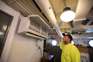 Caption: Glenn Davis, a heating and cooling technician with Jacksonville Heating Contractors, inspects a Carrier ductless air conditioner recently installed aboard the USS North Carolina.